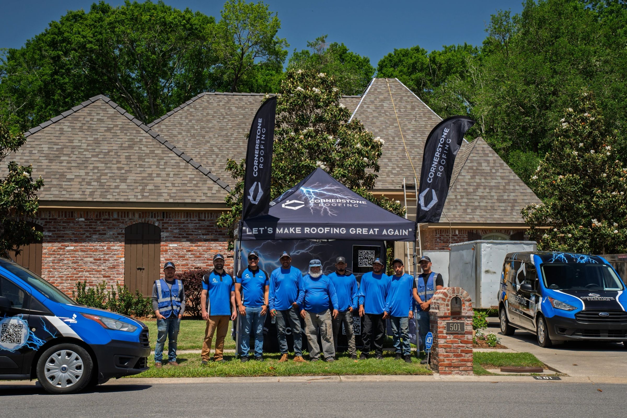 The full Cornerstone Roofing & Construction crew gathered in front of a home with Cornerstone flags and a branded vehicle